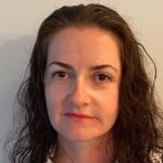 Individual with wavy brown hair and a white top stands against a neutral background, suitable for Medbridge's online healthcare education.