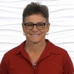 A smiling person with short hair and glasses wearing a red shirt stands against a textured white background, expressing enthusiasm for digital health technologies at medbridge.