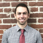 Person in gray shirt and red tie stands confidently in front of a brick wall, representing medbridge's future in digital healthcare.