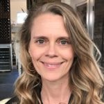 A confident woman with long, wavy blonde hair and a black top promotes hybrid care at Medbridge.