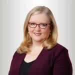A smiling person with blonde hair and glasses wears a burgundy blazer, embodying medbridge's blend of digital healthcare innovation and personal warmth.