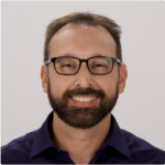 A smiling person with glasses, a beard, and a dark shirt represents the approachable nature of Medbridge's digital healthcare.