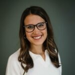 A person with long brown hair and glasses smiles, wearing a white shirt, representing medbridge's healthcare education.