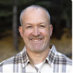 A smiling bearded man in a plaid shirt represents Medbridge's digital healthcare solutions outdoors.