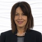 A smiling person with dark hair wears a pearl necklace, representing Medbridge's digital healthcare sophistication.