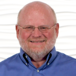 A bearded man with glasses smiles, representing digital healthcare innovation for medbridge.
