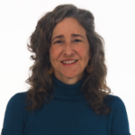 A curly-haired woman in a dark turtleneck smiles, representing the innovation of hybrid care in healthcare education with medbridge.