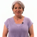 A short-haired person in a lavender top stands against a simple background.