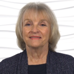 An elderly woman with grey hair in a dark sweater smiles warmly, capturing Medbridge's compassionate care spirit.