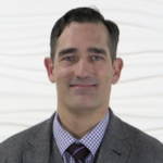Man in a suit with checkered shirt and tie against a textured white background for medbridge.