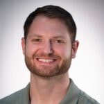 A man with short hair and a beard in a green shirt smiles confidently, representing healthcare education for medbridge.