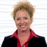 A person with curly hair smiles confidently, wearing a black blazer and red shirt, against a wavy white background, reflecting their passion for digital healthcare innovation at Medbridge.