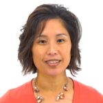 A person with short dark hair in a coral top and beaded necklace smiles at the camera.