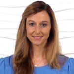 A woman with long brown hair smiles warmly, wearing a blue top against a white background, reflecting her interest in digital healthcare and Medbridge innovation.