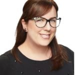 A smiling person with long brown hair and glasses, wearing a black top against a white background, represents hybrid care in medbridge healthcare education.