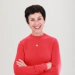 Smiling woman in a red sweater with short dark hair stands with arms crossed, representing medbridge.