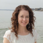 A woman with curly hair smiles by the sea, possibly contemplating digital healthcare advancements like medbridge.