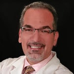 A man with glasses and gray hair in a white coat smiles in front of a black background, representing medbridge.