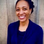 A smiling person in a dark blue top represents healthcare education in front of a wooden background for medbridge.