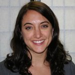 A smiling person with long, dark hair in a dark top stands against a light checkered background, symbolizing Medbridge's intersection of healthcare training and education.