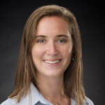 A person with long brown hair smiles in a professional headshot for medbridge, wearing a light blue shirt against a dark background.