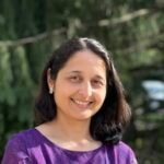 A person with shoulder-length dark hair, wearing a purple top, smiles outdoors, embodying their enthusiasm for healthcare education and digital innovation at medbridge.
