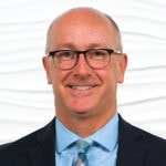 A smiling bald man in glasses and a suit represents Medbridge's digital healthcare future against a white background.