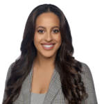 A smiling person with long dark hair in a grey plaid blazer poses against a white background for medbridge.