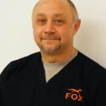 A bearded man wearing a black shirt with an orange logo stands confidently, representing medbridge's role in digital healthcare innovation.
