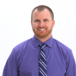 A bearded man in a purple shirt and striped tie smiles warmly, embodying medbridge's modern digital healthcare spirit.