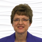 A smiling woman with short brown hair and glasses in a blue blazer represents Medbridge's digital healthcare initiatives.