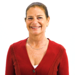A smiling person with dark hair in a red sweater stands against a white background, embodying medbridge's enthusiastic healthcare education.