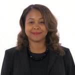 A woman with wavy brown hair in a black blazer smiles subtly, representing the professionalism of medbridge patient care software.