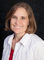 A woman with shoulder-length hair and a white blouse over a red top smiles against a dark background, representing digital healthcare innovation at medbridge.