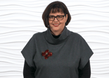 A woman with short brown hair and glasses, wearing a gray top with a red flower brooch, represents digital healthcare innovation in front of a white background for medbridge.