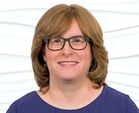 A person with shoulder-length hair and glasses smiles warmly, embodying hybrid care in a blue top against a white background for medbridge.