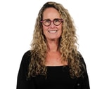 Woman with long curly blonde hair and glasses, in black top, stands against a white background, representing medbridge excellence.