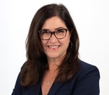 Smiling woman with long brown hair and glasses, wearing a navy blazer, representing medbridge.