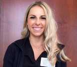 A woman with long blonde hair and a name badge smiles in front of a wooden background, representing medbridge healthcare education.