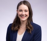 Woman in navy blazer and white top smiles at camera, representing medbridge's innovative approach to digital healthcare.