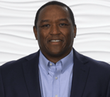 A man in a suit and blue shirt smiles against a white background, representing Medbridge's digital healthcare innovation.