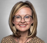 A smiling woman with glasses and dangling earrings wears a patterned top, embodying enthusiasm for modern healthcare education, representing medbridge.