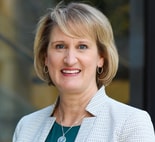 A smiling person with short blonde hair and a patterned blazer represents medbridge's digital healthcare innovations.