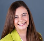 Woman with long brown hair in a bright green blazer smiles before a gray background, symbolizing innovation at medbridge.
