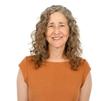 A smiling woman with curly gray hair and an orange top stands against a white background, embodying medbridge's approachability.
