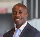 A man in a suit smiles at the camera indoors, representing professionalism in digital healthcare at medbridge.