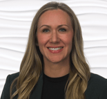 Woman with long blond hair smiling in a black shirt and dark jacket before a wavy white backdrop.