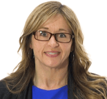 A smiling woman with blond wavy hair and glasses wears a blue top and black jacket against a white background, representing medbridge.