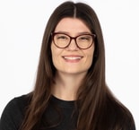 A woman with long brown hair and glasses smiles at the camera, representing digital healthcare for medbridge.