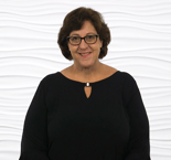 A smiling woman with short brown hair and glasses wears a black top, representing Medbridge’s innovative approach to hybrid healthcare education.